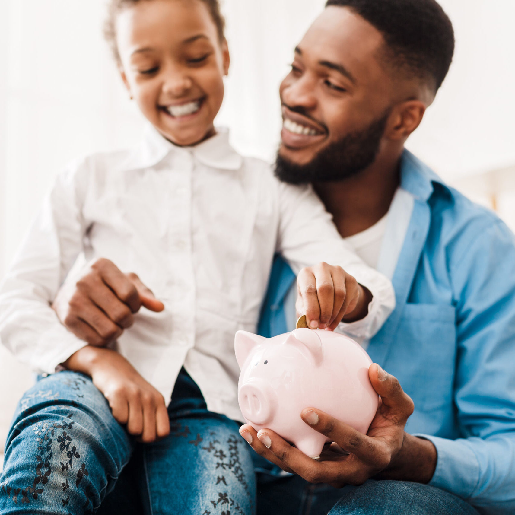 Girl and father putting coin into piggy bank, sitting on sofa at home